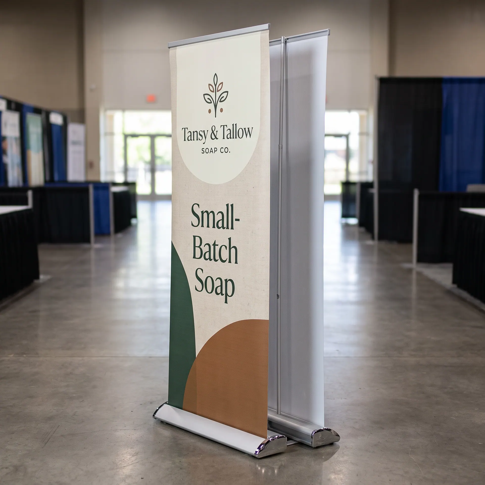 Double-sided retractable banner stand, one base carrying a printed graphic on each face, shown with a sample design: in the middle of a convention aisle, seen at an angle that shows both faces